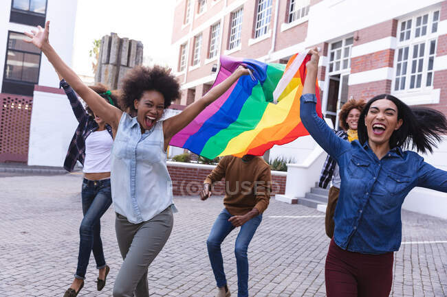 Diversos manifestantes masculinos y femeninos en marcha sosteniendo la bandera del arco iris, vitoreando con los brazos levantados. marcha por la igualdad de derechos y justicia. - foto de stock