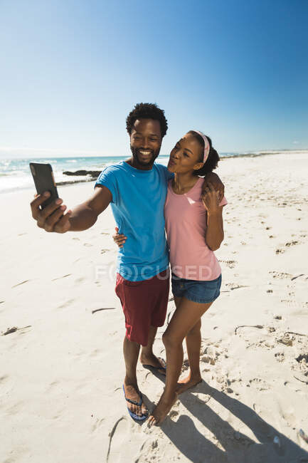 Happy african american couple on beach by the sea taking selfie. healthy outdoor leisure time by the sea. — Stock Photo