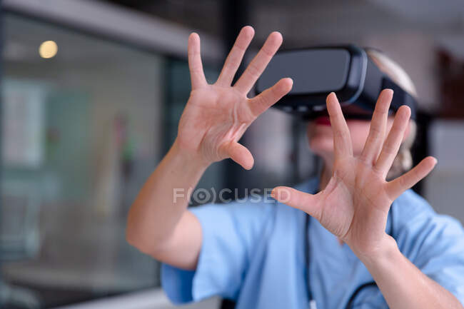 Caucasian female doctor wearing scrubs using vr headset and virtual interface. medical professional at work with technology. — Stock Photo