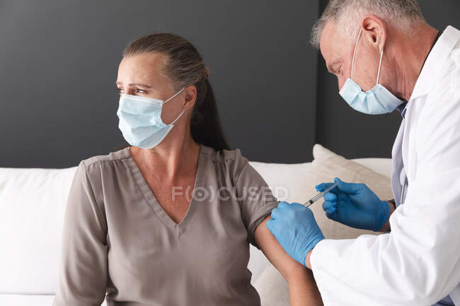 Médecin homme âgé caucasien vaccinant une patiente covid 19, tous deux portant un masque facial. professionnel de la santé au travail pendant une pandémie de coronavirus covid 19. — Photo de stock