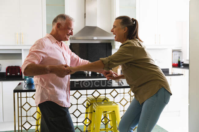 Счастливая старшая кавказская пара на кухне, веселые танцы и улыбки. оставаться дома в изоляции во время карантинной изоляции. — стоковое фото