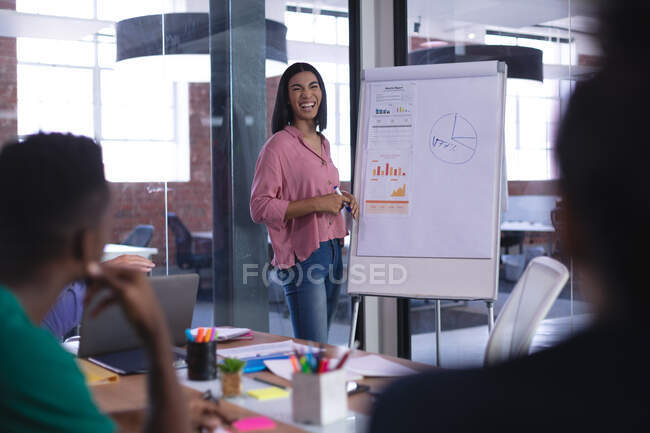 Mulher de negócios de raça mista em pé no quadro branco dando apresentação a grupo diversificado de colegas. negócio de design criativo independente. — Fotografia de Stock