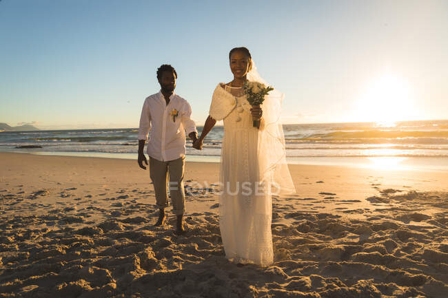 Африканская американская пара, влюбленная в брак, гуляющая по пляжу, держась за руки. любовь, романтика и пляжный свадебный летний отдых. — стоковое фото
