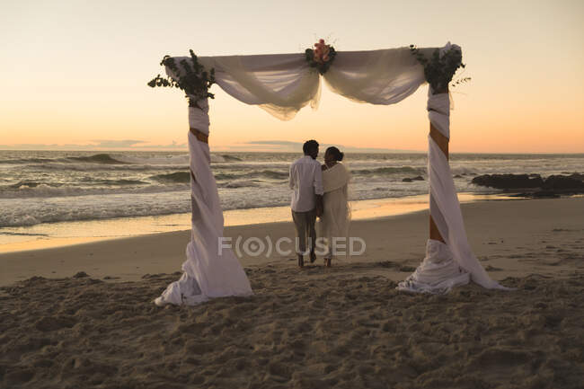 Африканская влюбленная пара выходит замуж, гуляя по пляжу во время заката, держась за руки. любовь, романтика и свадебный пляжный отдых. — стоковое фото