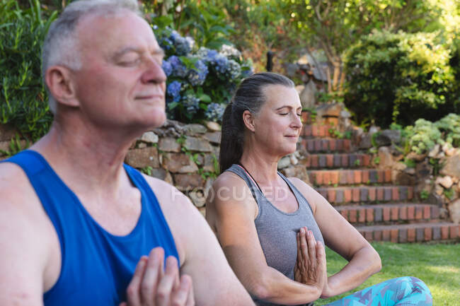 Счастливая старшая кавказская пара в саду практикующая йогу, сидящая и медитирующая. оставаться дома в изоляции во время карантинной изоляции. — стоковое фото