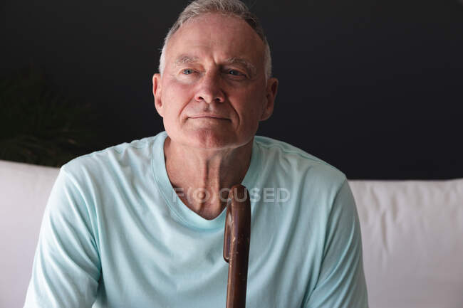 Кавказький старший чоловік у вітальні сидить на дивані думаючи тримаючи палицю. Перебуваючи вдома в ізоляції під час карантину.. — стокове фото