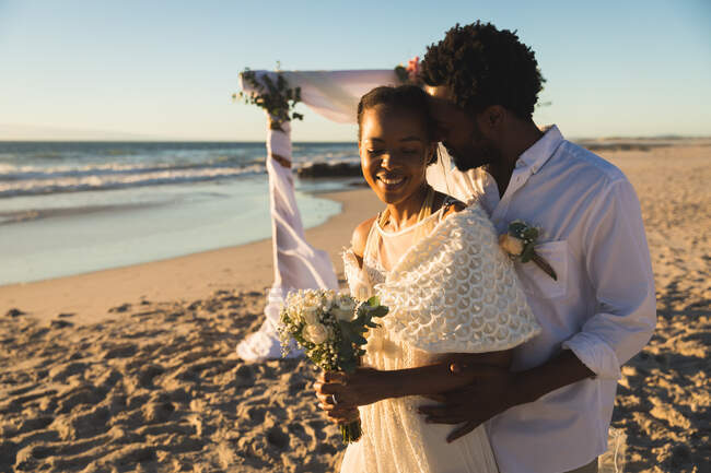 Счастливая африканская американская пара влюблённая выходит замуж, обнимается на пляже во время заката. романтика и отдых на пляже. — стоковое фото