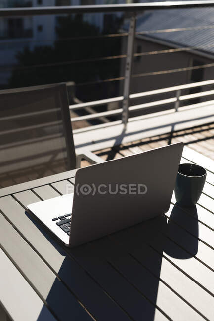 Ноутбук і чашка кави на столі на сонячній терасі даху. Перебуваючи вдома в ізоляції під час карантину.. — стокове фото