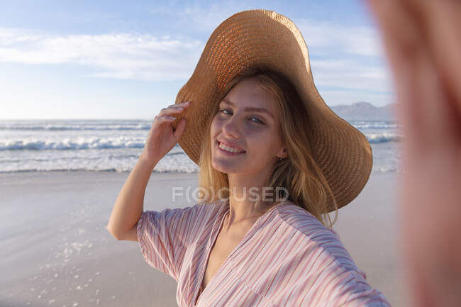 Mulher branca usando chapéu tirando uma selfie na praia. tempo de lazer ao ar livre saudável pelo mar. — Fotografia de Stock