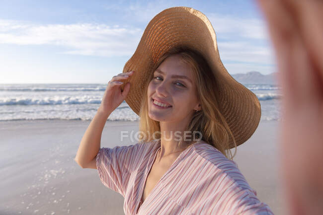 Caucasian woman wearing hat taking a selfie at the beach. healthy outdoor leisure time by the sea. — Stock Photo