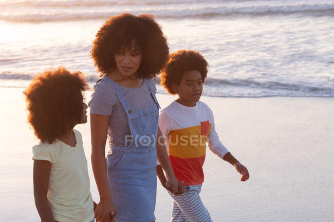 African american mother and two children walking and holding hands at the beach. healthy outdoor leisure time by the sea. — Photo de stock