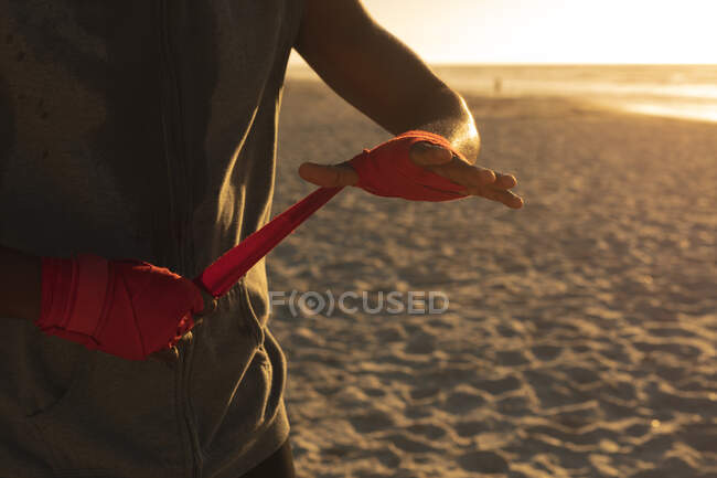 African american man exercising outdoors wrapping hands in preparation for training at sunset. healthy outdoor lifestyle fitness training. — Stock Photo