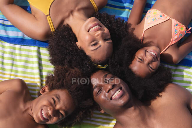 Ritratto di genitori afroamericani e due bambini sdraiati su un asciugamano sulla spiaggia sorridenti. famiglia tempo libero all'aperto vicino al mare. — Foto stock