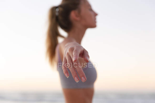 Mulher caucasiana realizando exercícios de alongamento em pé na praia. fitness ioga e conceito de estilo de vida saudável — Fotografia de Stock