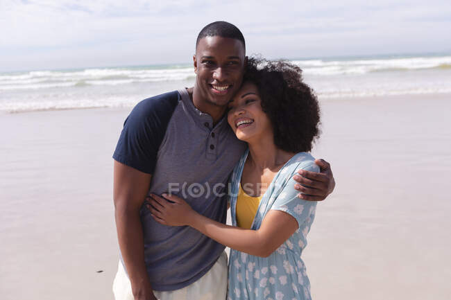 African american couple standing and embracing at the beach smiling. healthy outdoor leisure time by the sea. — Fotografia de Stock