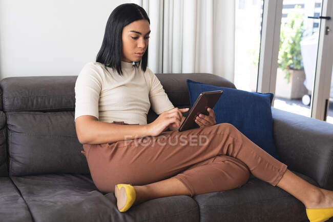 Mixed race transgender woman relaxing in living room sitting on couch using tablet. staying at home in isolation during quarantine lockdown. — Stock Photo