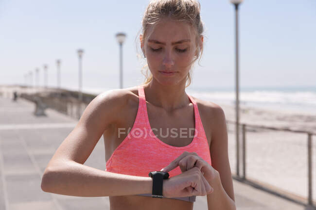 Caucasian woman exercising using her smartwatch on a promenade by the beach. healthy outdoor leisure time by the sea. — Stock Photo