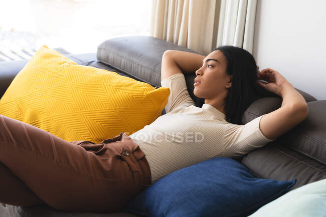 Glückliche Transgender-Frau mit gemischter Rasse entspannt sich im Wohnzimmer auf der Couch liegend. Isolationshaft während der Quarantäne. — Stockfoto