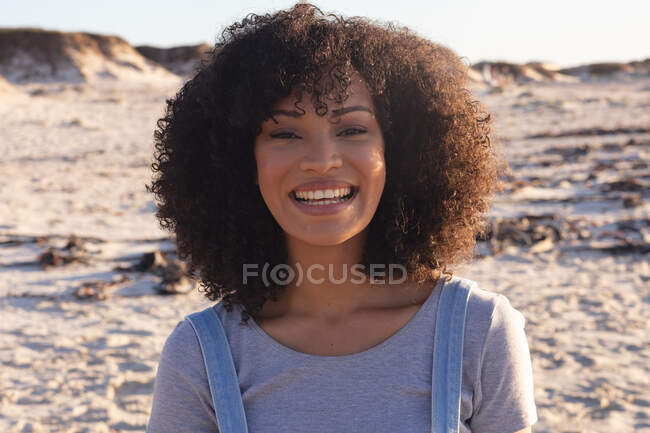 Портрет афро-американської жінки, яка дивиться на камеру і посміхається на пляжі. Здоровий вільний час на відкритому повітрі біля моря. — стокове фото