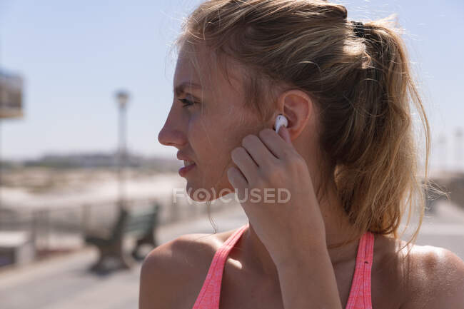 Mulher caucasiana se exercitando colocando fone de ouvido em um passeio pela praia. tempo de lazer ao ar livre saudável pelo mar. — Fotografia de Stock