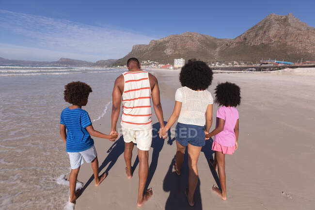 African american parents and two children walking and holding hands at the beach. family outdoor leisure time by the sea. — Stock Photo