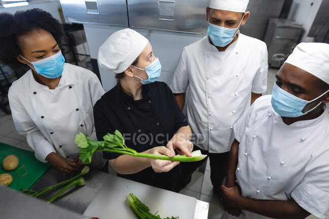 Divers chefs professionnels masculins et féminins préparant des légumes portant des masques faciaux. travailler dans une cuisine de restaurant occupé pendant coronavirus covid 19 pandémie. — Photo de stock