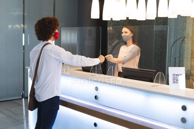 Разнообразный бизнесмен в маске для лица разговаривает с секретаршей в отеле. отель для деловых поездок во время пандемии коронавируса. — стоковое фото