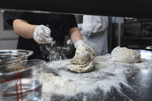 Der mittlere Teil des professionellen Küchenchefs knetet Teig mit Hygienehandschuhen. Arbeit in einer belebten Restaurantküche. — Stockfoto