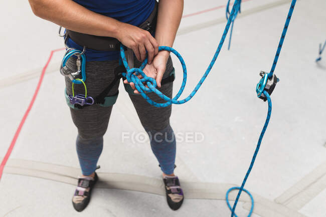 Midsection of woman knotting rope in a harness belt at indoor climbing wall. fitness and leisure time at gym. — Stock Photo