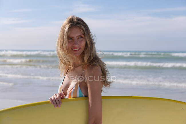 Smiling caucasian woman wearing bikini carrying yellow surfboard at the beach. healthy outdoor leisure time by the sea. — Fotografia de Stock