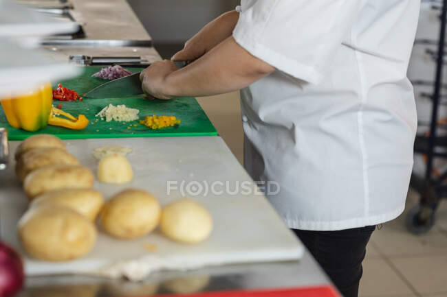 Midsection of professional chef preparing vegetables with knife. working in a busy restaurant kitchen. — Stock Photo