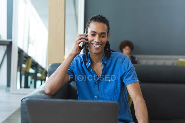 Portrait of mixed race businessman sitting on sofa talking on smartphone. casual meeting in business lounge. — Stock Photo