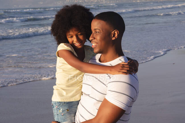 African american father and daughter embracing and smiling at the beach. family outdoor leisure time by the sea. — Stock Photo