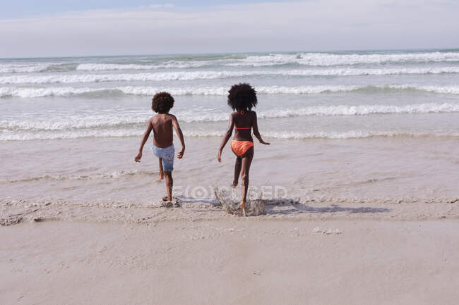African american children running at the beach towards the sea. family outdoor leisure time by the sea. - foto de stock