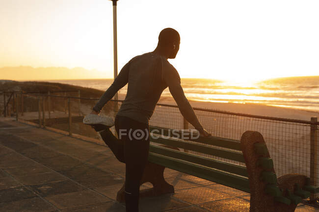 Homem afro-americano exercitando-se ao ar livre, estendendo-se na ponte ao pôr do sol. treinamento de fitness ao ar livre saudável. — Fotografia de Stock