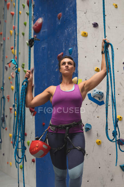 Белая женщина, держащая веревки и готовясь к восхождению на крытую скалолазную стену. фитнес и досуг в тренажерном зале. — стоковое фото