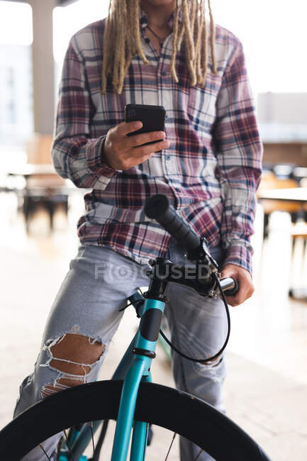 Midsection of mixed race man with dreadlocks sitting on bicycle in street using smartphone. digital nomad, out and about in the city. — Stock Photo