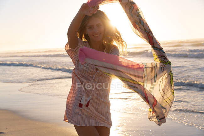 Porträt einer kaukasischen Frau mit Schal, die am Strand steht und lächelt. Sommerferienkonzept. — Stockfoto