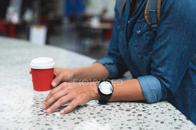 Sección media de la mujer sosteniendo la taza de café en el mostrador. fitness y tiempo libre en el gimnasio durante coronavirus covid 19 pandemia. - foto de stock