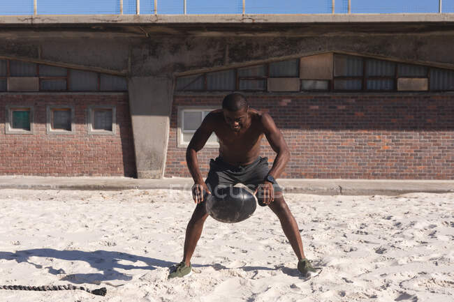 Afrikanisch-amerikanischer Mann, der an sonnigen Tagen am Strand mit Gewichten trainiert. gesundes Outdoor-Fitness-Training. — Stockfoto