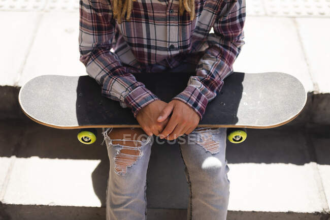 Parte média do macho sentado nas escadas com skate na rua. estilo de vida urbano verde, fora e sobre na cidade. — Fotografia de Stock