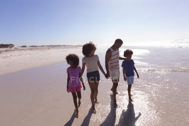 Afrikanisch-amerikanische Eltern und zwei Kinder beim Gehen und Händchenhalten am Strand. Familienfreizeit im Freien am Meer. — Stockfoto
