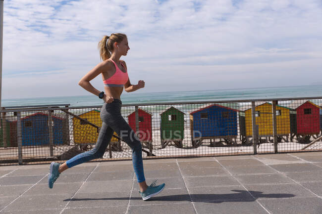 Caucasian woman exercising jogging on a promenade by the beach. healthy outdoor leisure time by the sea. — Stock Photo