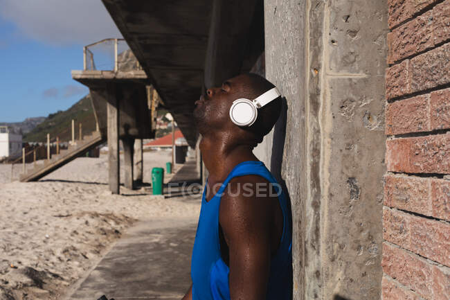 Hombre afroamericano haciendo ejercicio al aire libre, usando auriculares, escuchando música. estilo de vida al aire libre saludable entrenamiento fitness. - foto de stock