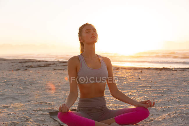 Кавказка на пляже, практикующая йогу, сидящая в медитации. здоровье и благополучие, отдых на пляже на рассвете. — стоковое фото