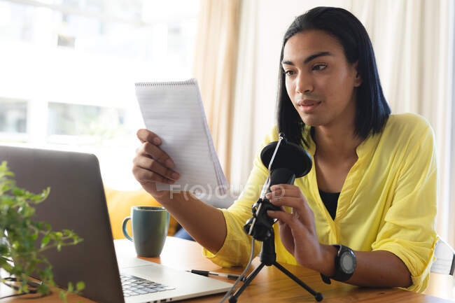 Mulher transgênero mista fazendo podcast usando microfone e laptop, lendo notas. ficar em casa em isolamento durante o confinamento de quarentena. — Fotografia de Stock