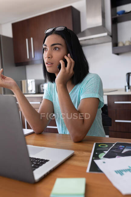 Mulher transgênero de raça mista trabalhando em casa usando laptop falando no smartphone. ficar em casa em isolamento durante o confinamento de quarentena. — Fotografia de Stock
