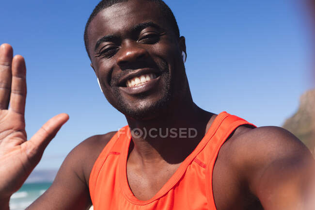 Retrato de um homem afro-americano sorridente a exercitar-se, acenando para a câmara. treinamento de fitness ao ar livre saudável. — Fotografia de Stock