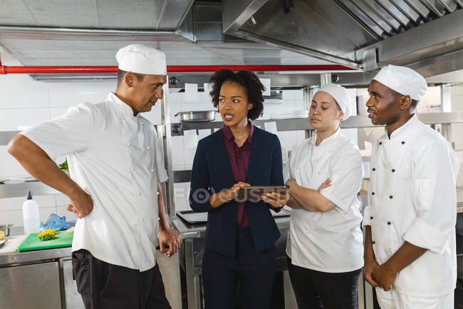Diverso grupo de chefs profesionales que se reúnen con el gerente de cocina. trabajando en una cocina ajetreada. - foto de stock