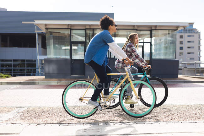 Zwei gemischte Männerfreundinnen fahren Fahrräder auf der Straße und unterhalten sich. grüner urbaner Lebensstil, unterwegs in der Stadt. — Stockfoto